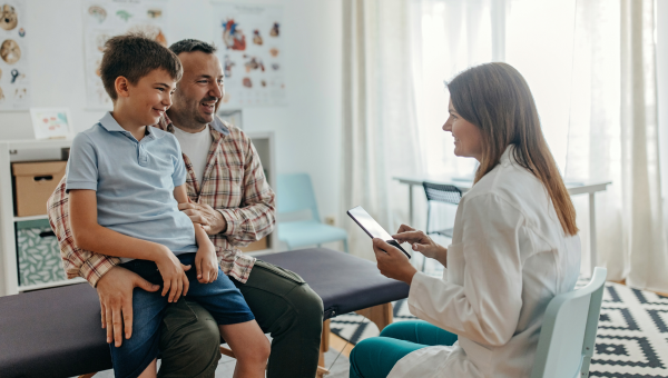 boy sits on his dad's lap on an exam table talking to a doctor during an ADHD evaluation