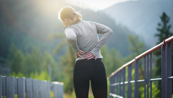 closeup of a woman from behind, clutching her lower back in pain while on an outdoor run