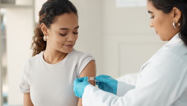 young healthy woman with a nurse placing a bandaid on her arm after a flu shot