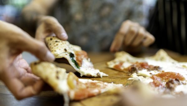 view of pizza on a table, multiple hands pulling out a slice