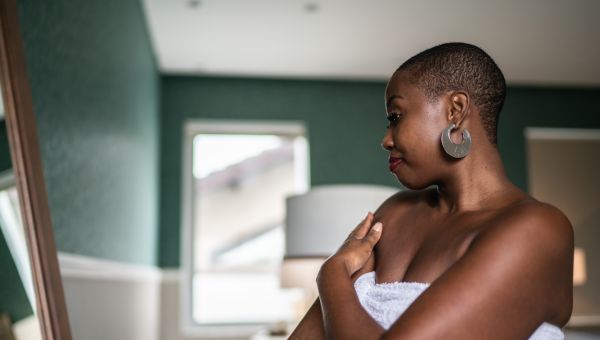 woman in towel looking in the mirror in her bedroom doing a self exam for skin cancer