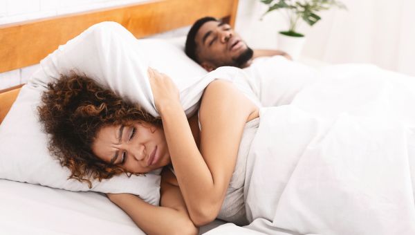 annoyed woman laying in bed next to snoring husband