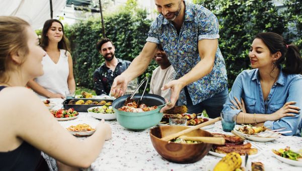 a diverse group of mixed race young adults gathers for a group dinner in a backyard