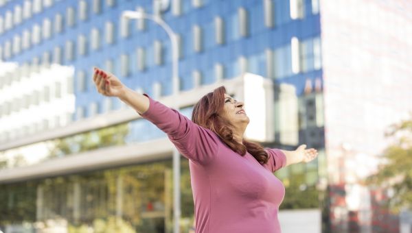overweight person walking outside in a city and raising their arms upwards