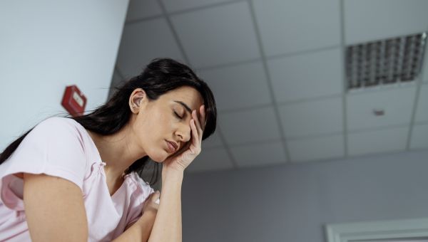 Someone in a hospital gown, holding their head with a headache