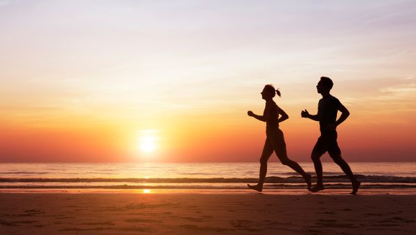 A couple slimming down for the summer by running on the beach.