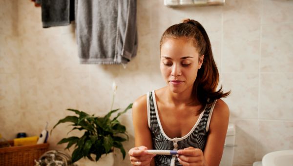 a young Black woman looks at a home pregnancy test