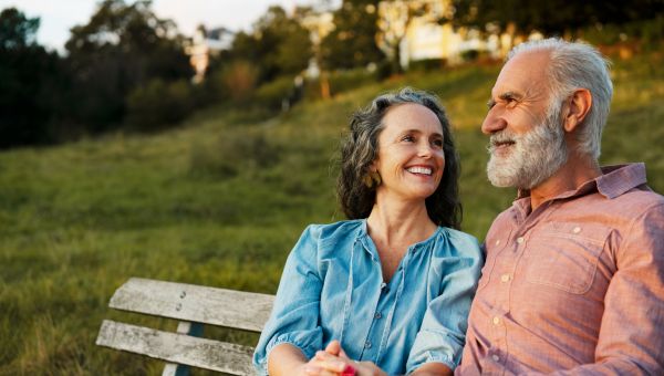a healthy happy middle aged White couple sits on a park bench at sunset