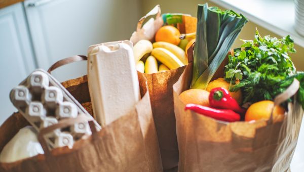 paper bags full of healthy fresh produce and other groceries sit on the kitchen counter