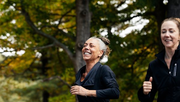 a middle aged gray haired white woman smiles as she goes on a jog with her friend, a younger white woman