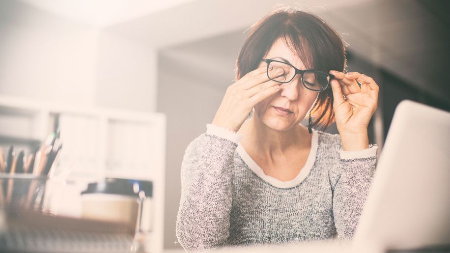 Woman with a headache rubbing her eyes in front of a computer.