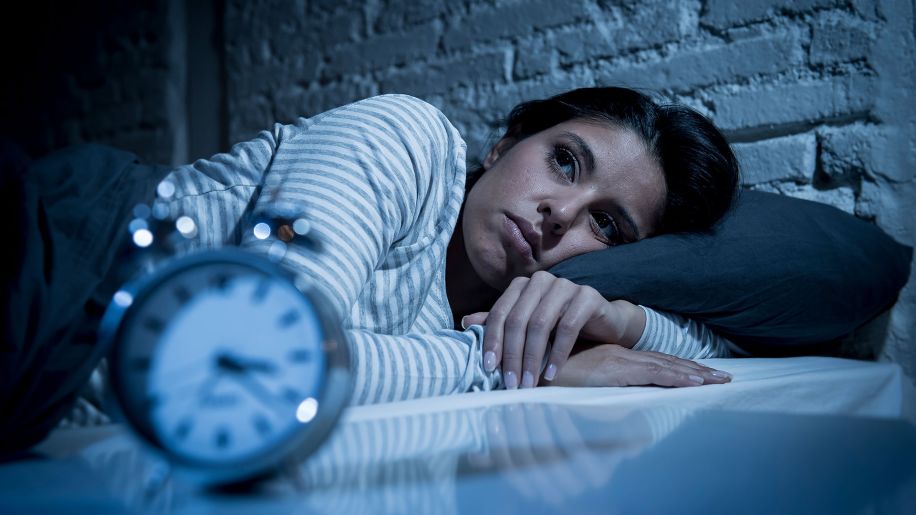 Woman lies awake in bed with clock nearby.