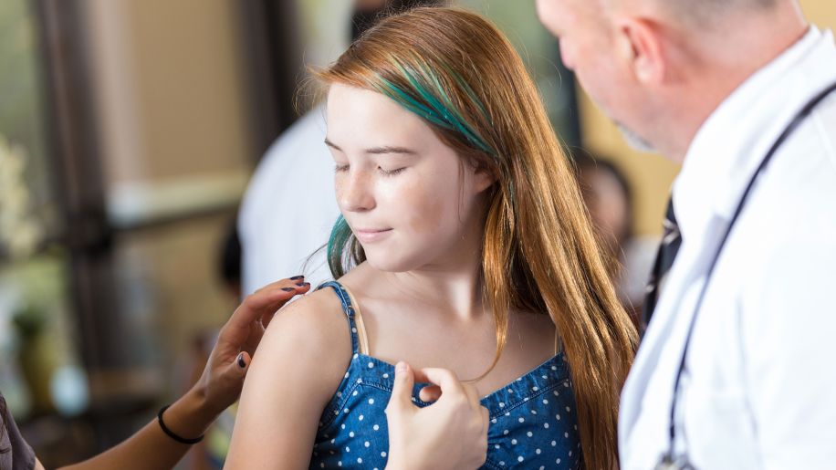 Preteen with red hair receiving a vaccine from a certified nurse