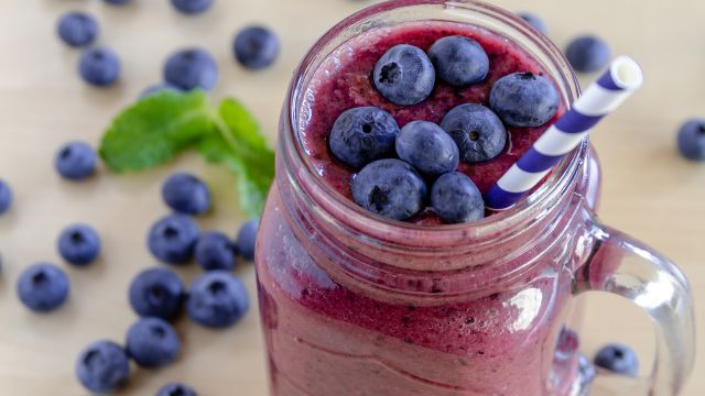 Mason jar filled with blueberry and blackberry fresh fruit smoothie sitting on counter with bowl of blueberries