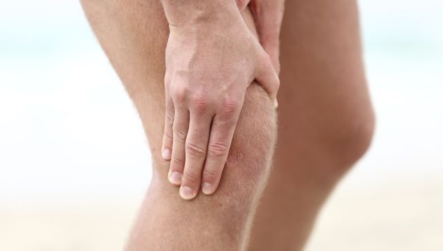 A man with cartilage deterioration in his knee grips the damaged knee in pain. 