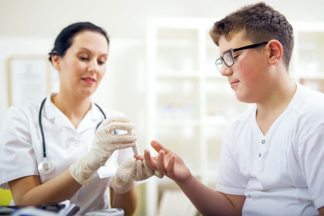 A nurse checks for diabetes in a teen by taking blood from his finger. 
