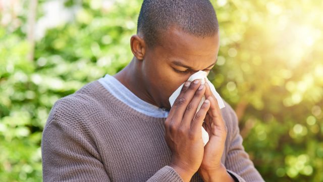 young man blowing his nose outdoors