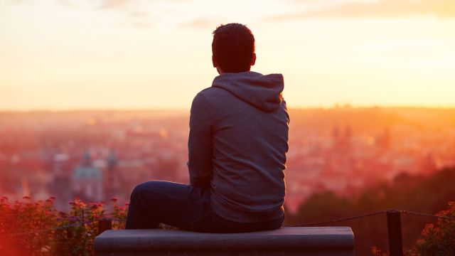 lonely young man staring out at city at sunset