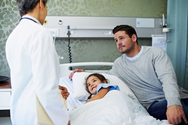 girl in hospital bed with father and doctor