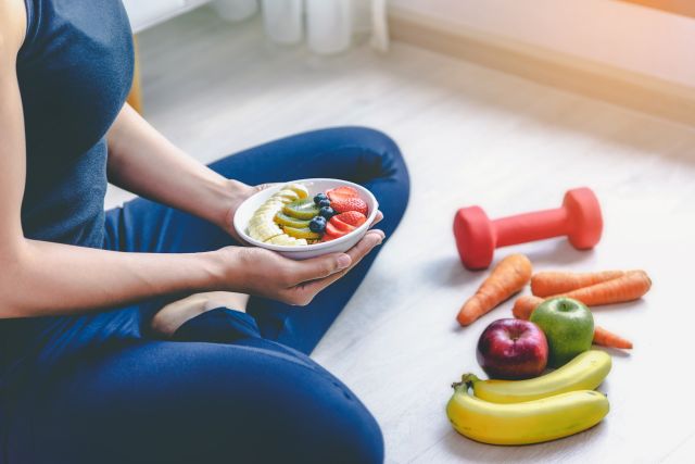 woman sitting by exercise equipment holding bowl of fruit 