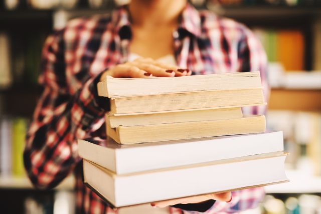 A young woman holds a stack of books. Understanding key terms related to endometriosis can be helpful to patients.