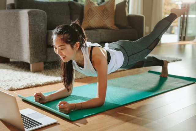 Woman holding plank while streaming workout on laptop at home