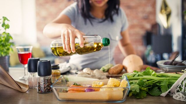 A woman uses a healthy, high-smoke-point cooking oil to prepare her salmon and corn before she cooks dinner.