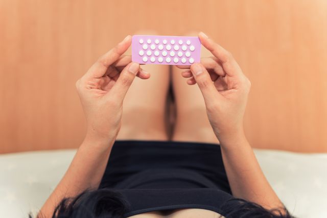 Woman holding a birth-control pill package, one of several potential treatments for heavy periods