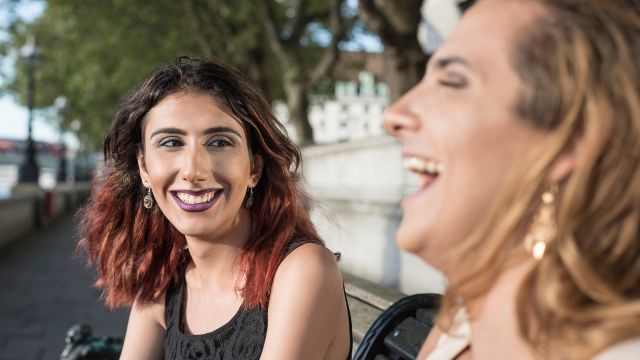Two transgender female friends hanging out and laughing outdoors.
