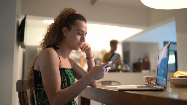 Young woman using a phone and laptop on a dining room table