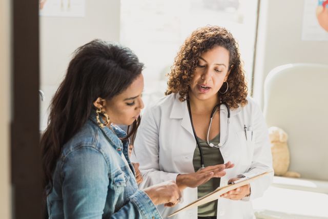 a female doctor and her female patient discuss a medical record on a clipboard