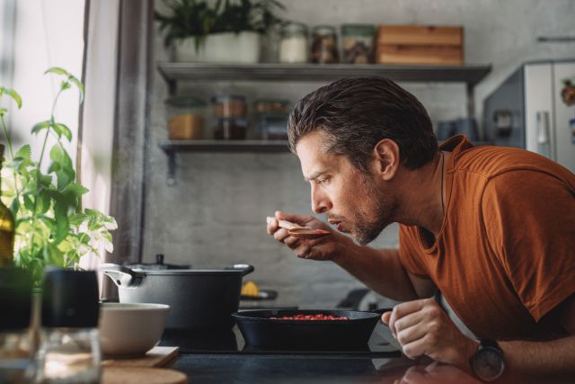 fit-looking man tastes a healthy soup he's cooking in his kitchen