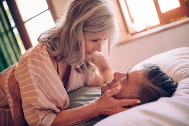 mature couple looking into each other's eyes with desire while lying down in bed