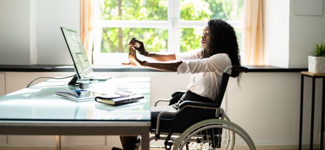 Young black businesswoman sitting in a wheelchair at a desk and stretching her hands and arms