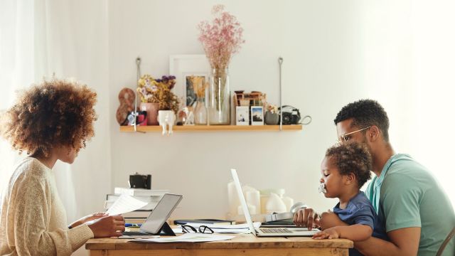 A man and woman working at kitchen table with child