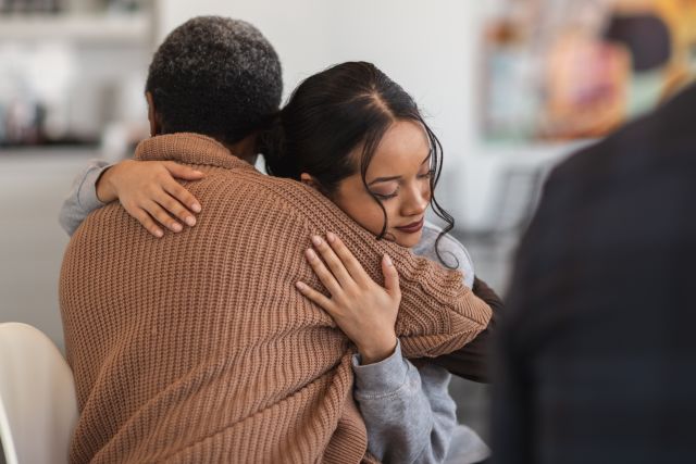 a young mixed-race woman hugs a Black woman during a group support session