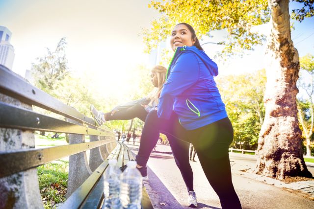 a Latina and Black woman in workout wear stretch after a running workout in the park