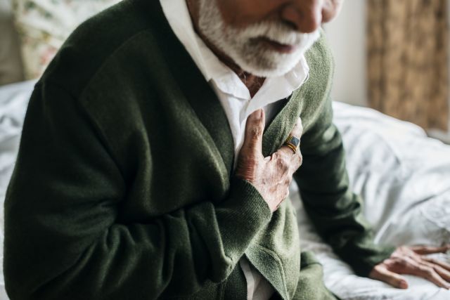 man in green sweater clutching chest