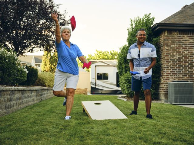 an older white woman and a middle aged South Asian man play a game of backyard cornhole