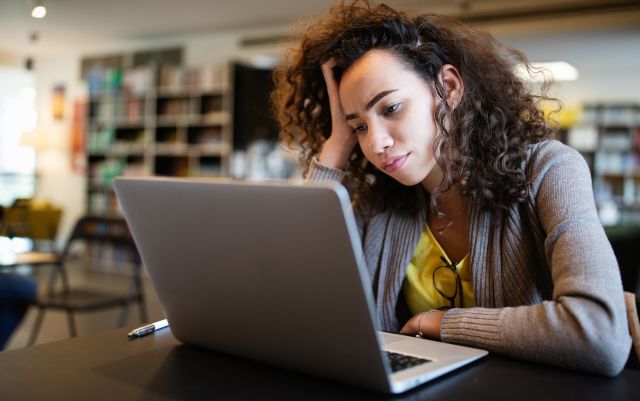 teen girl worried about adhd stares at open laptop at desk in school library