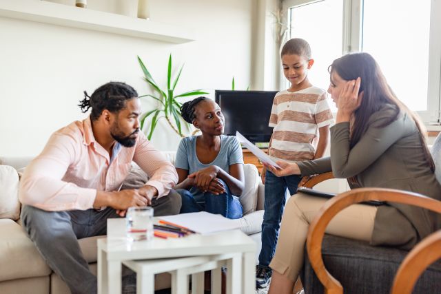 parents sit on a sofa next to standing young son listening to therapist talk about adhd treatment