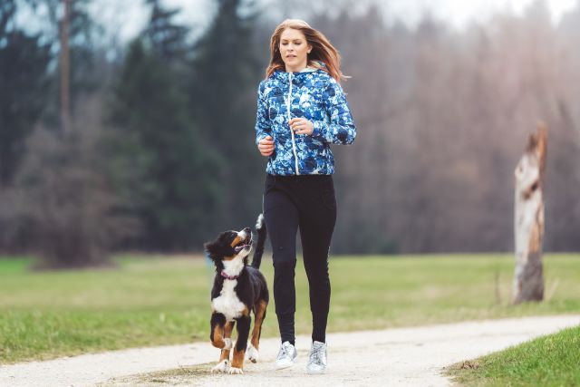 A woman living with adult ADHD walks down a park trail with her dog, getting exercise and relaxing, to minimize his symptoms.