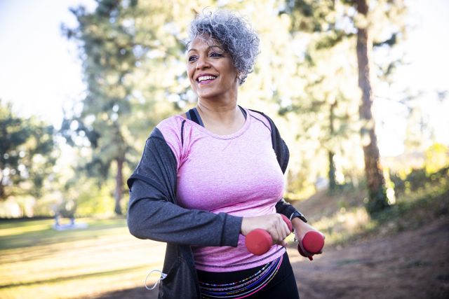 Senior Black Woman with Knee Pain Stretching and Exercising with Weights in the Park