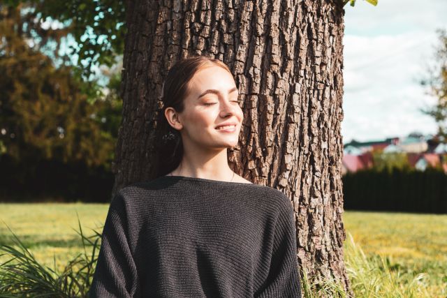 Young woman leaning on tree enjoying the warm sunlight. 