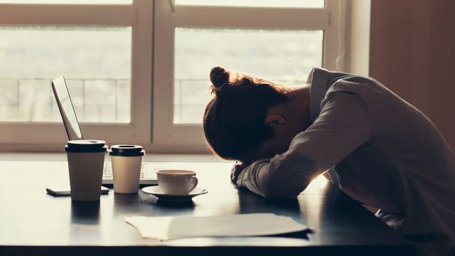 A woman with anemia fatigue rests her head in front of her laptop despite drinking three coffees. 