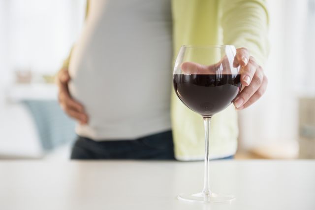 pregnant person pouring glass of red wine down the sink