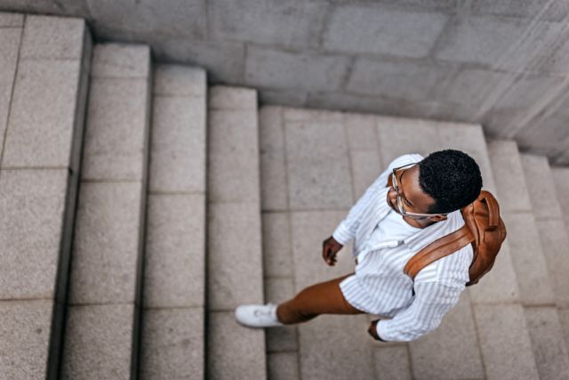 Top view of young person wearing eyeglasses with backpack walking upstairs in city while commuting to work