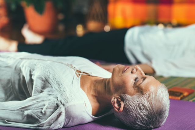 Senior who suffers from chronic pain lies on her back on the floor with her eyes closed to meditate