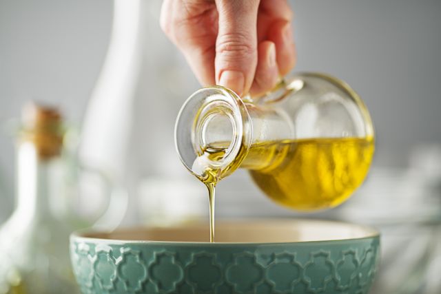 hand pouring olive oil from a glass pitcher into a ceramic bowl
