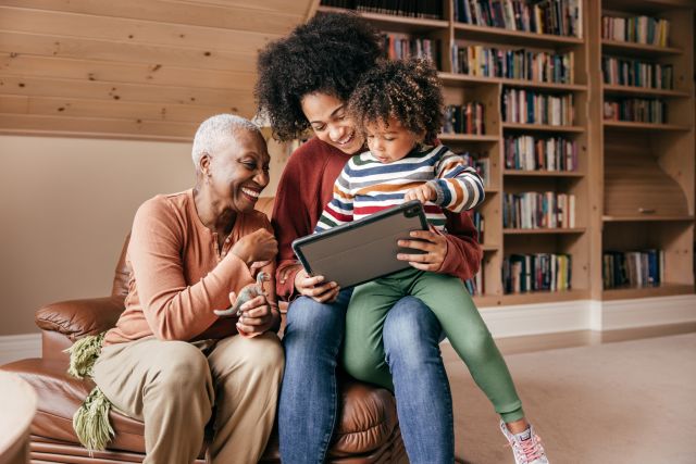 a multi-generational Black family enjoys time together: a grandmother, mother, and child view a tablet